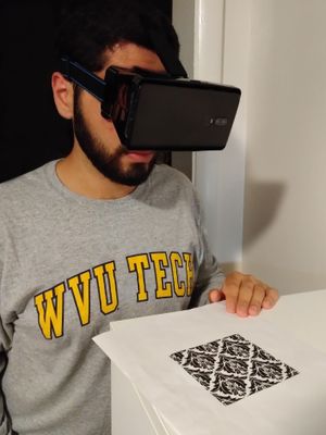 WVU Tech student Nima ShahabShahmir wears a set of AR goggles as he looks down at a piece of paper with a pattern printed on it.