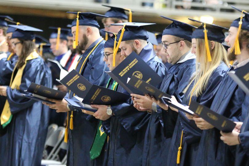 WVU Tech graduates stand in their blue caps and gowns, programs open in front of them, as they sing the University's alma mater.