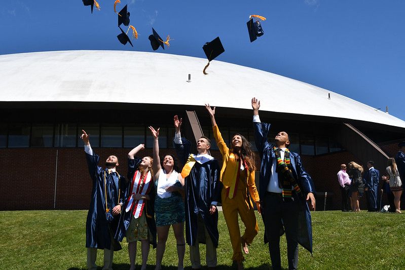 Six recent Tech grads toss their graduation caps into the air on a sunny spring day, the convention center behind them and not a cloud in the sky.