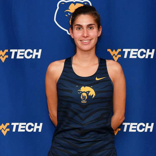 A young woman in a blue tank top with the Golden Bear logo on it stands in front of a blue WVU Tech backdrop.