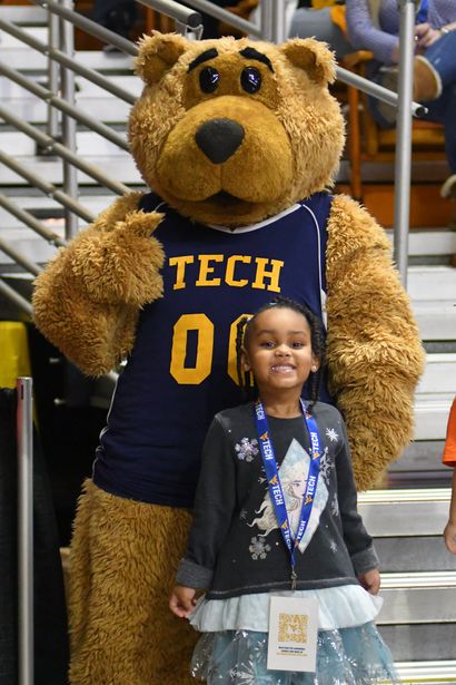 A young girl standing next to a bear mascot
