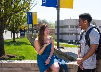 two students talking, with campus buildings in the background
