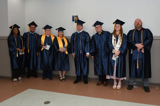 A group of eight RBA students in their graduation regalia stand in the Raleigh County Convention Center.