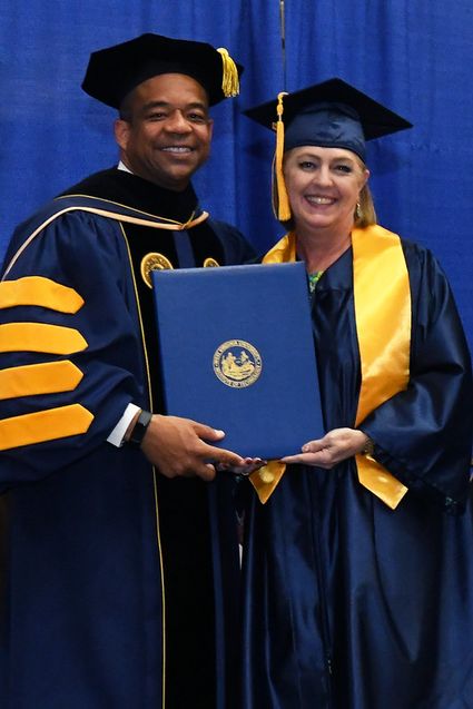 Dr. T. Ramon Stuart in graduation regalia stands with Janie Smith in graduation regalia, holding her diploma.