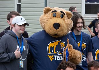 Monty the Golden Bear Mascot standing next to two students posing for a photo