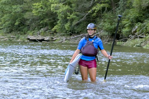 Melanie Seiler in a blue life jacket holding a paddleboard and paddle in a river